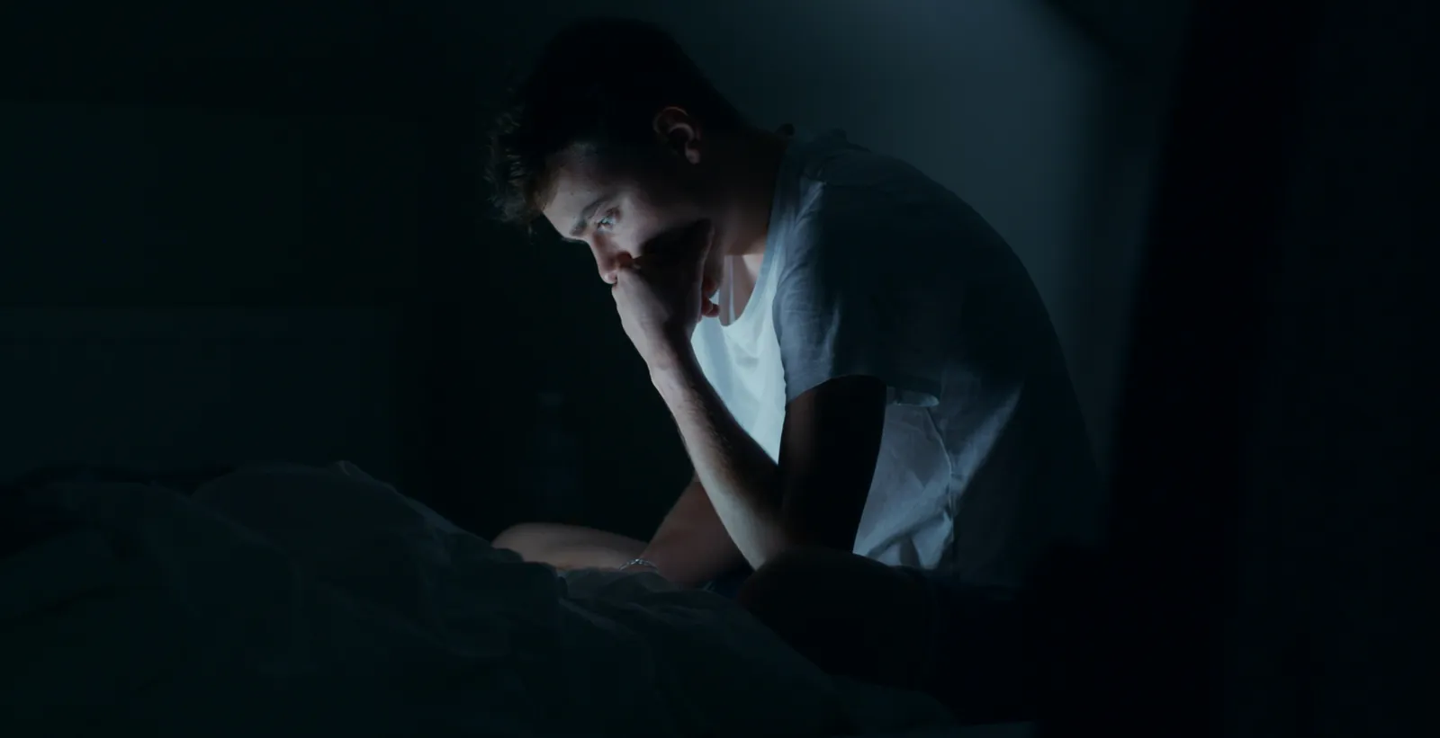 Hombre sentado en la cama de noche, a oscuras, sin poder dormir