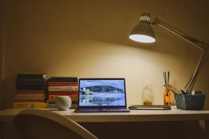 Escritorio iluminado de noche con papeles y un portátil, imagen sobre el sobreesfuerzo en el síndrome del impostor